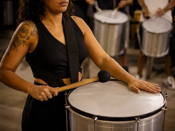 Percussionista mulher tocando surdo com uma mão na baqueta e outra abafando a pele